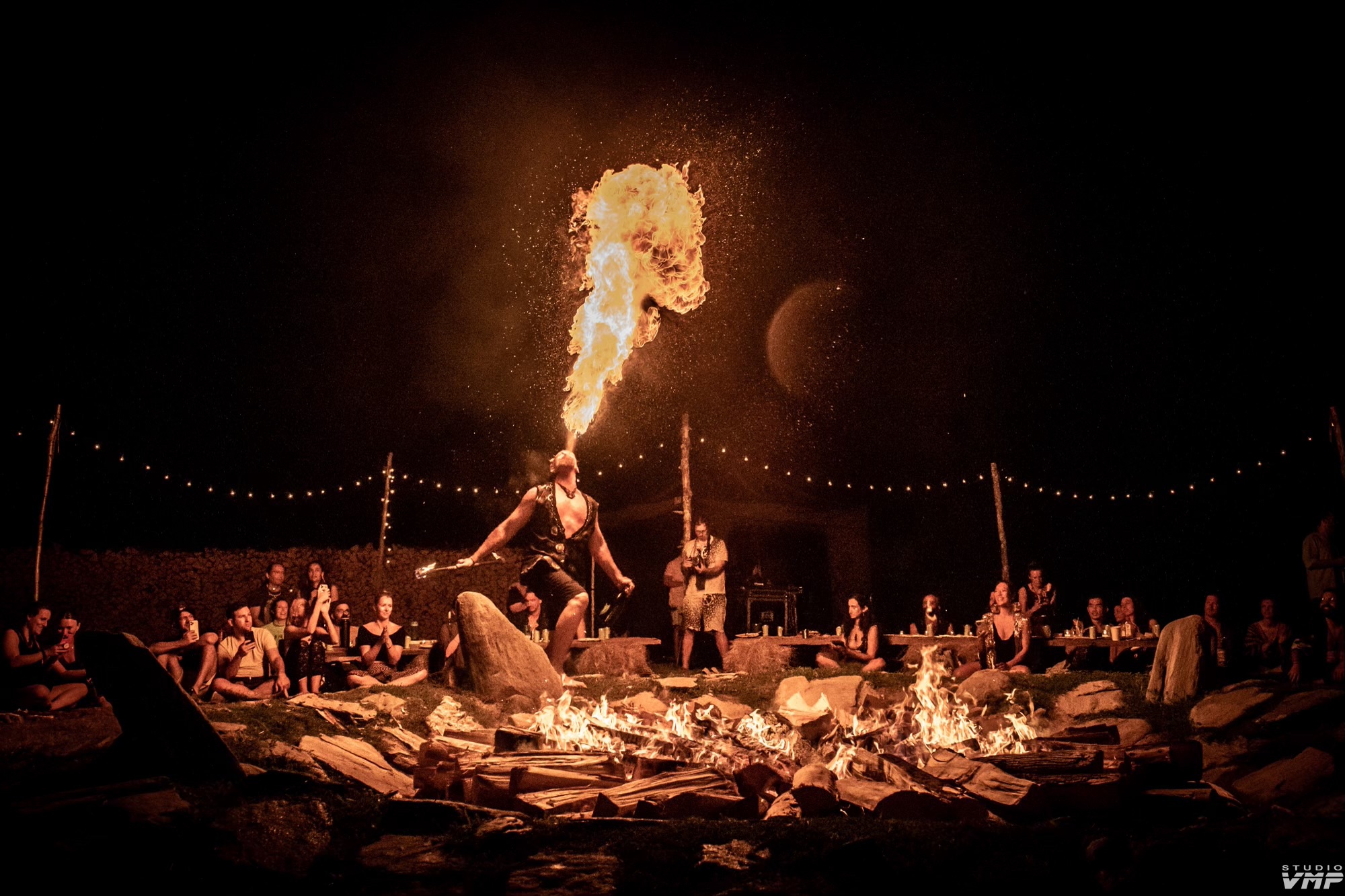 A fire performer surrounded by an audience at an outdoor evening event; photograph by Studio VMP