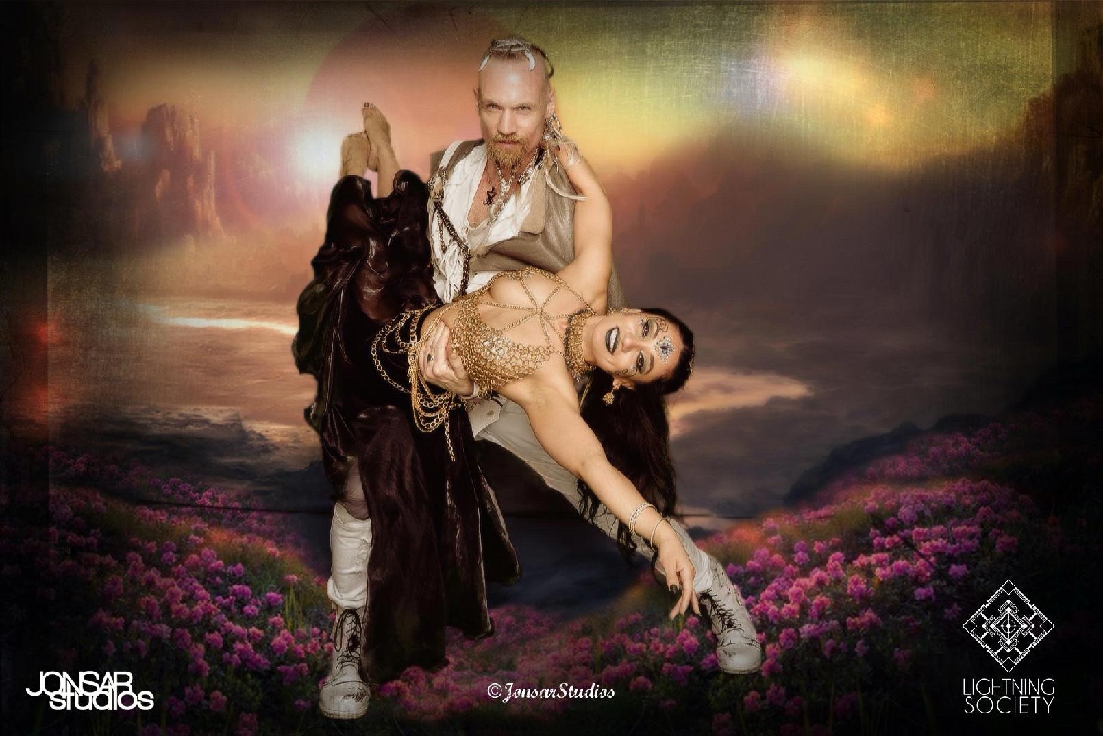John and Radhika in a theatrical portrait against a fantasy landscape